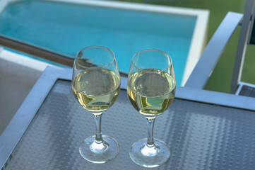 Two wine glasses with white wine and swimming pool on the background
