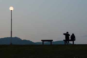 Silhouette of two people sitting bench on top of the mountain view background.