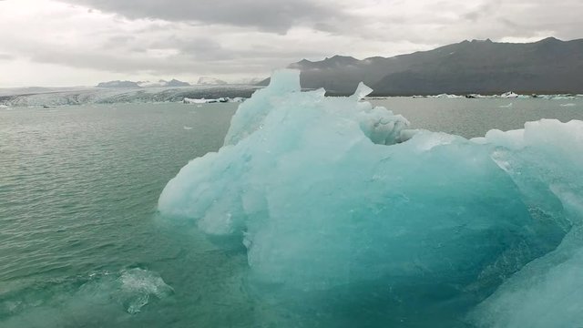 The camera flies over one of the most beautiful natural sights of Iceland, the ice of Jökulsarlon. A blue glacier can be seen in a close up pan.