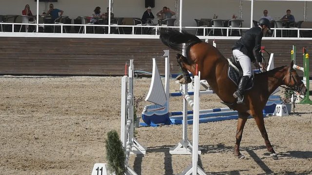 Unrecognizable professional male jockey rides on horseback. Horse is galloping and jumping through a barrier in competition. Slow motion Side view Close up