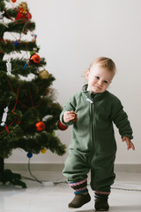 Boy dressed in warm green jumpers stands before Christmas tree