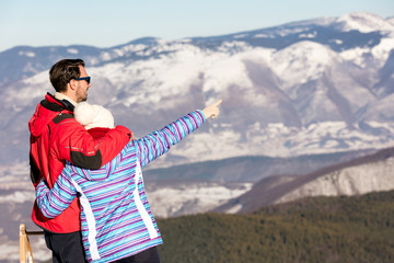 Rear view of a loving couple in fur hood jackets looking at snowed mountain range