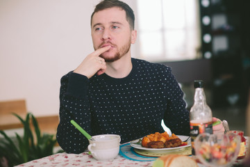 Thoughtful man in spotted sweater sits at dinner table