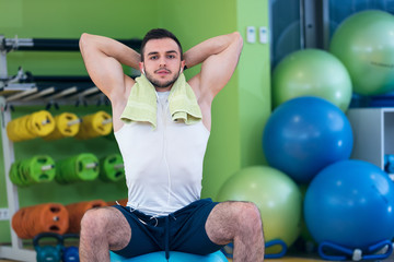 Male athlete kneeling down by dumbbells toweling sweat of his brow.