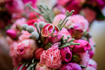 Wedding ring made of yellow and white gold lie on bouquet of pink peonies and roses