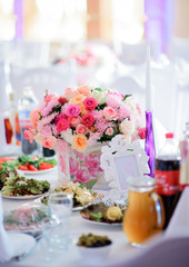 Bouquet made of pink roses stands in the middle of dinner table served with salads