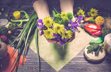 Graceful hands of the woman florist  making bouquet of bright irises on a wooden table. Workplace of the florist and accessories. Vintage retro toning