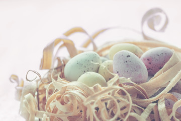 Coloured eggs in nest made from wood shavings close up, selective focus. Warm pastel toned photo