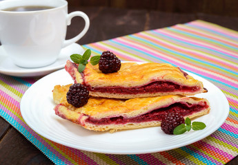 Pieces of sweet berry pie on the white plate and cup of tea on the bright napkin.