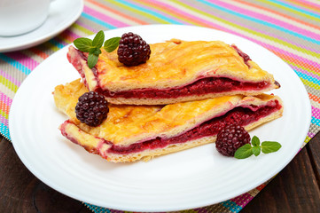Pieces of sweet berry pie on the white plate and cup of tea on the bright napkin. Close up