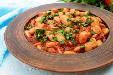 White large beans in sweet and sour tomato sauce in a clay bowl on a light background. Vegetarian cuisine. Lenten meal. Close up
