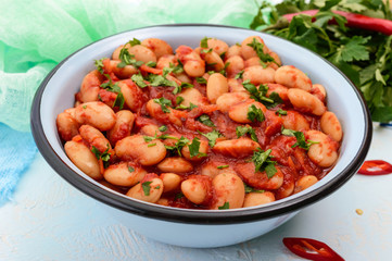 White large beans in sweet and sour tomato sauce in a bowl on a light background. The top view. Vegetarian cuisine. Lenten meal.