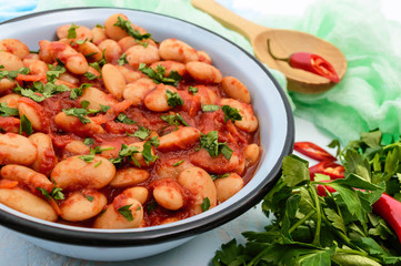 White large beans in sweet and sour tomato sauce in a bowl on a light background. The top view. Vegetarian cuisine. Lenten meal. Close up