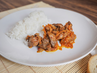 Scene with snow white ceramic dish of rice and roast meat, stew, meats with vegetables on a bamboo napkin on a wooden table from the old boards. Slices of white bread on the white paper napkins