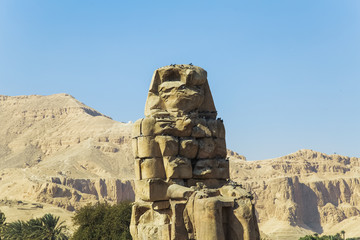 Ancient Colossi of  Memnon against mountains and blue sky background in Luxor, Egypt. Horizontal color photo.