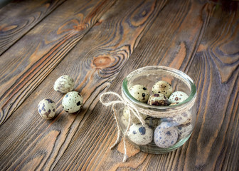 Fresh quail eggs in a glass jar,decorated with a linen rope, kitchen wooden table.