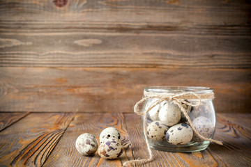Fresh quail eggs in a glass jar,decorated with a linen rope, kitchen wooden table.