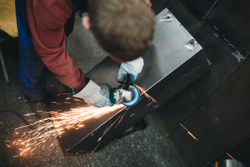 Metallurgy industry. Factory for production of heavy pellet stoves and boilers. Manual worker welder on his job. Extremely dark conditions and visible noise. Focus on foreground.