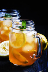 Black ice tea with lemon in a glass jar on a dark background, selective focus