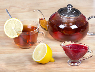 Стеклянная чашка и чайник с чаем,лимон и чашка с вареньем.