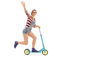 Cheerful female hipster riding a scooter and waving