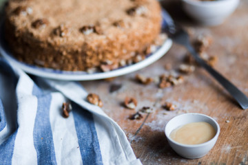 round delicious honey cake in blue white plate on a brown wooden background, bright flour, walnuts with white blue striped tea towel Golden amber honey with a fork