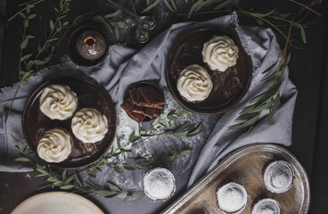 chocolate cupcakes with white cream and muffins in brown ceramic plate, chocolate spoons in black wooden table with tea towel with green food photo close-up