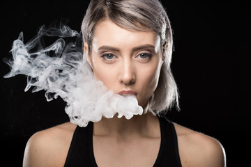 Attractive young woman vaping and blowing smoke on black © LIGHTFIELD STUDIOS
