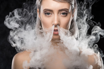 portrait of woman in bodysuit exhaling smoke on black