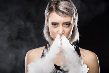 Young woman vaping and blowing smoke of electronic cigarette from nose