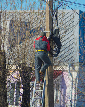 worker electrician repairs wires on the street pole standing on the stairs.