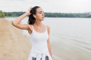 Beautiful fit female athlete girl on beach of lake in park. Listen and enjoy the music on her...