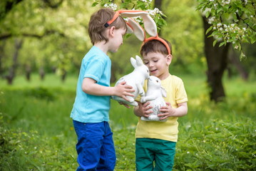 Obraz premium Two little kids boys and friends in Easter bunny ears during traditional egg hunt in spring garden, outdoors. Siblings having fun with finding colorful eggs. Old christian catholoc tradition