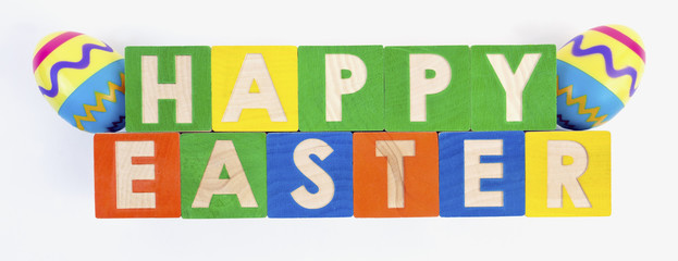 HAPPY EASTER greeting spelled with colorful toy blocks with decorated plastic eggs. 