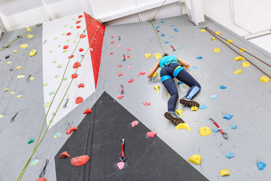 Young woman climbing up on practice wall at indoors gym, rear view