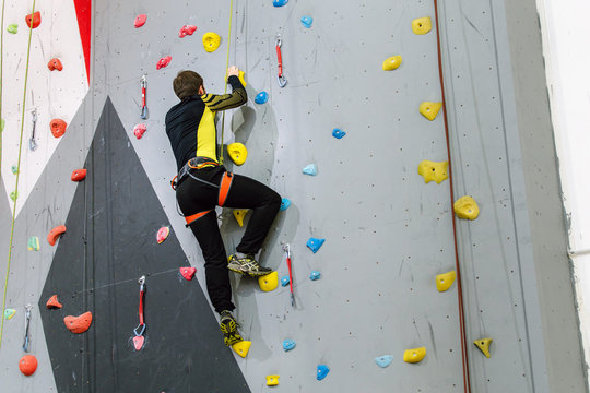 man climbing on practical wall indoor, with belay carabiners and rope