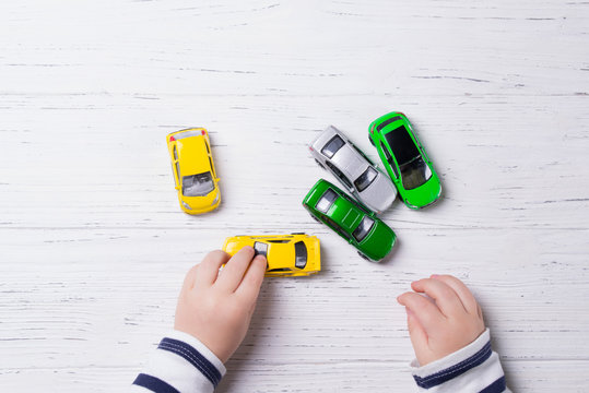 Child Hands Playing With Miniature Toy Cars, Wooden Background, Top View