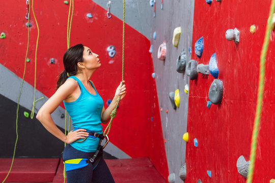 Young woman with belay rope practicing at rock-climbing on a artificial climb wall indoors
