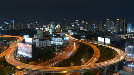 Fototapeta na wymiar Long Exposure Aerial Nighttime Urban View of Motion Blur Traffic on Roads Comprising a Stack Interchange with a Modern City High Rise Skyline in the Background - Note Billboard Ads have been Blurred