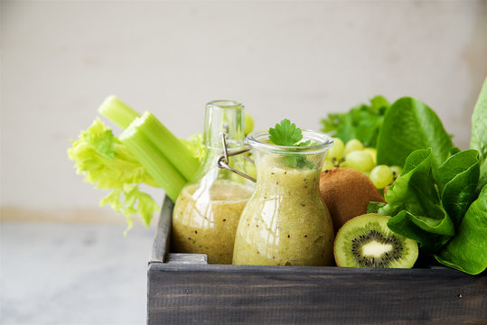 Green smoothie with apples, kiwi, grapes, lettuce romano and parsley in bottles and wooden box on gray marble background