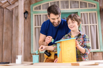 Low angle view of happy father and son painting wooden birdhouse on porch