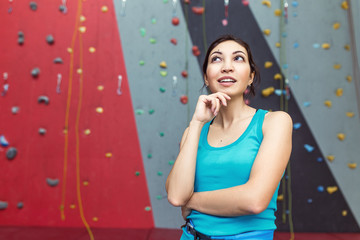 Female climber looking and thinking on artificial climbing wall background