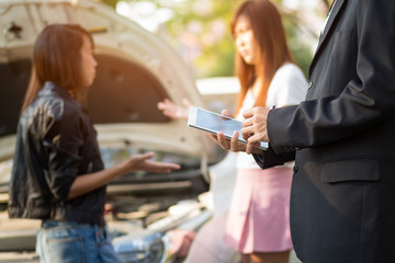 Side view of insurance agent  writing on tablet while examining car after accident