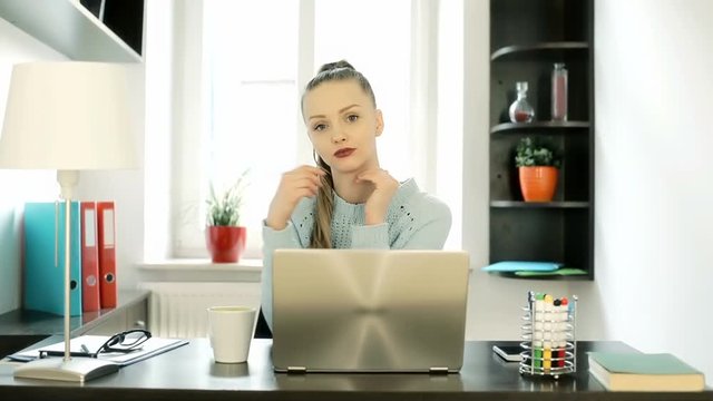 Attractive woman looking to the camera and drinking coffee in her office, steadycam shot

