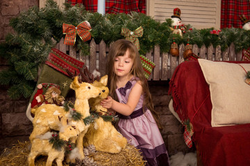 Little girl in a New Year's decorations near toy reindeer