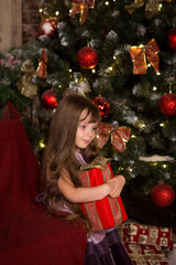 Girl near a Christmas tree with a gift in their hands