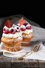 Muffins with soft cream and fresh raspberry powdered with sugar and decorated with chocolate, rustic background