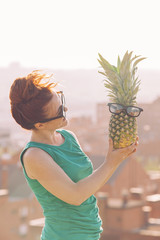 red hair woman looking at a pineapple with glasses.