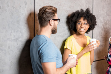 Multi ethnic coworkers dressed casually having a coffee break near the gray wall indoors