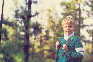 happy little boy with backpack travel in green forest